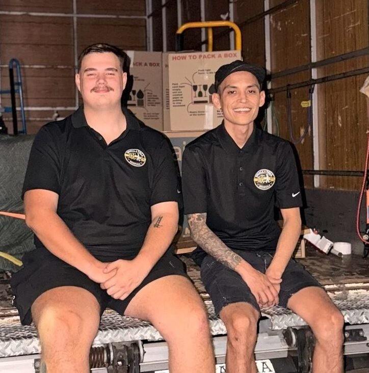Two Small & Tall Removals crew members in branded shirts, sitting on the truck tailgate at the end of a job